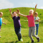 summer childhood leisure people concept group happy kids playing tag game running green field outdoors scaled e1705552377390