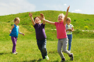 summer childhood leisure people concept group happy kids playing tag game running green field outdoors scaled e1705552377390