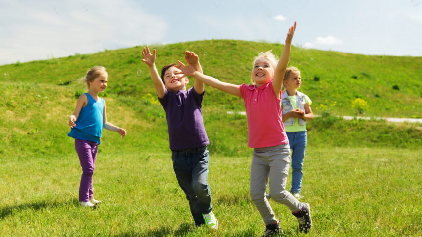 summer childhood leisure people concept group happy kids playing tag game running green field outdoors scaled e1705552377390